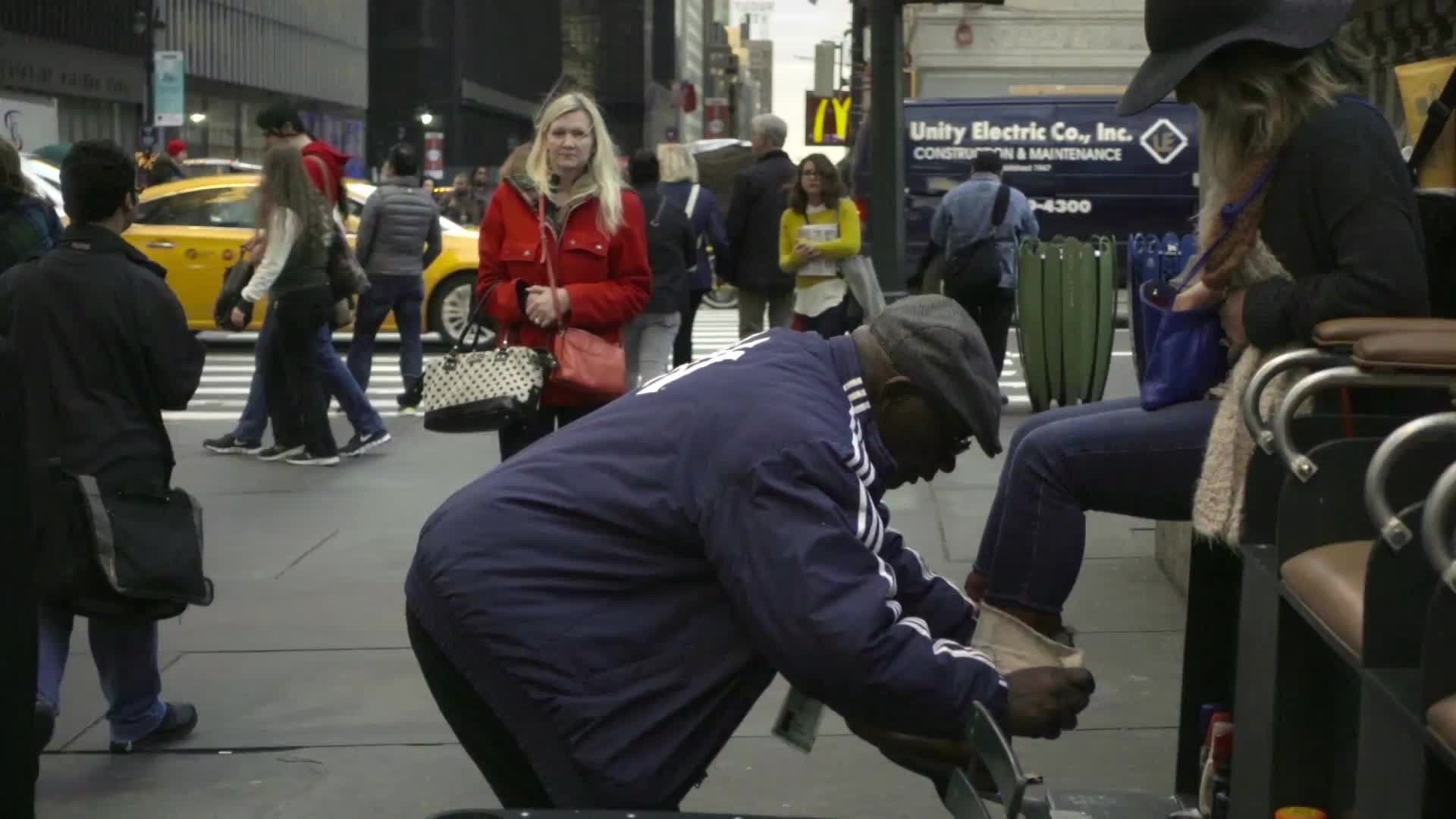 shoe shiner in Yankee jacket shining woman's boots on 42nd st and 5th avenue on crowded street during day, slow motion Manhattan NYC